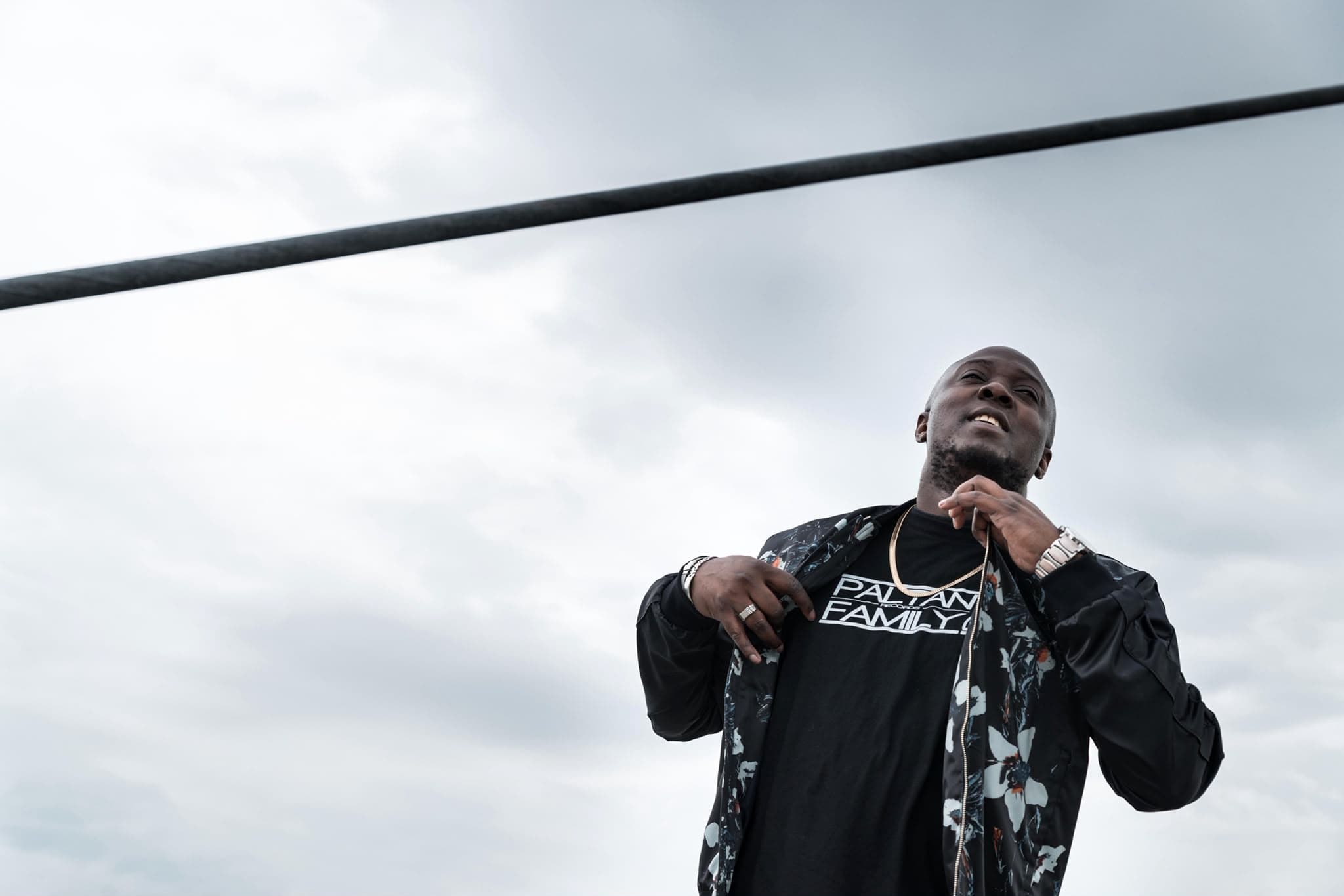 Black Moz en contre-plongée sous un ciel nuageux, t-shirt Paltan Family Records