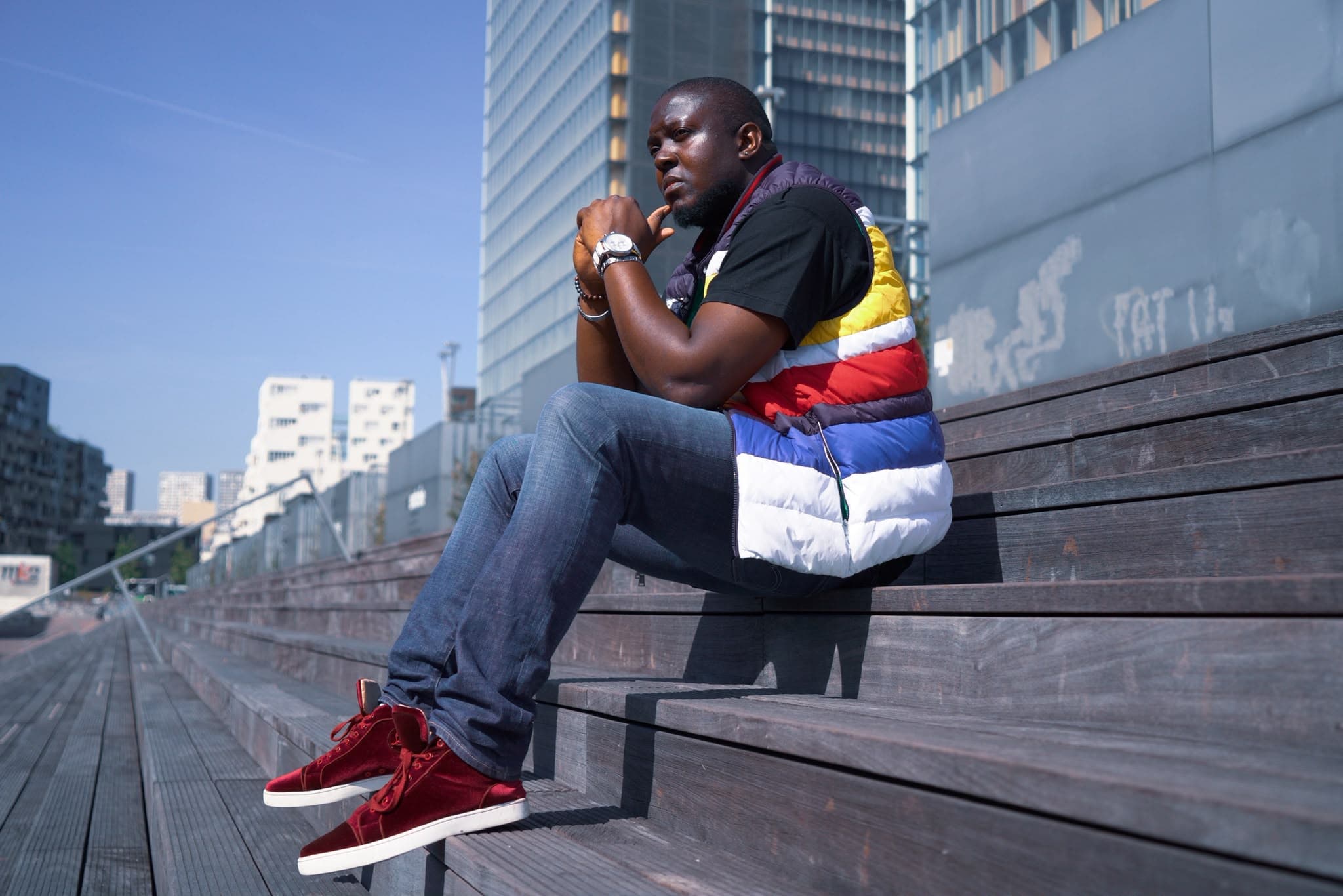 Black Moz assis sur des gradins en bois dans un décor urbain parisien